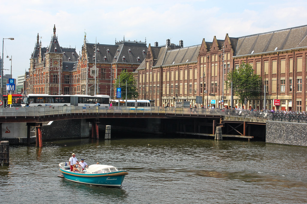 Barco navegando en el canal frente a la Estación Central de Ámsterdam en un día soleado.