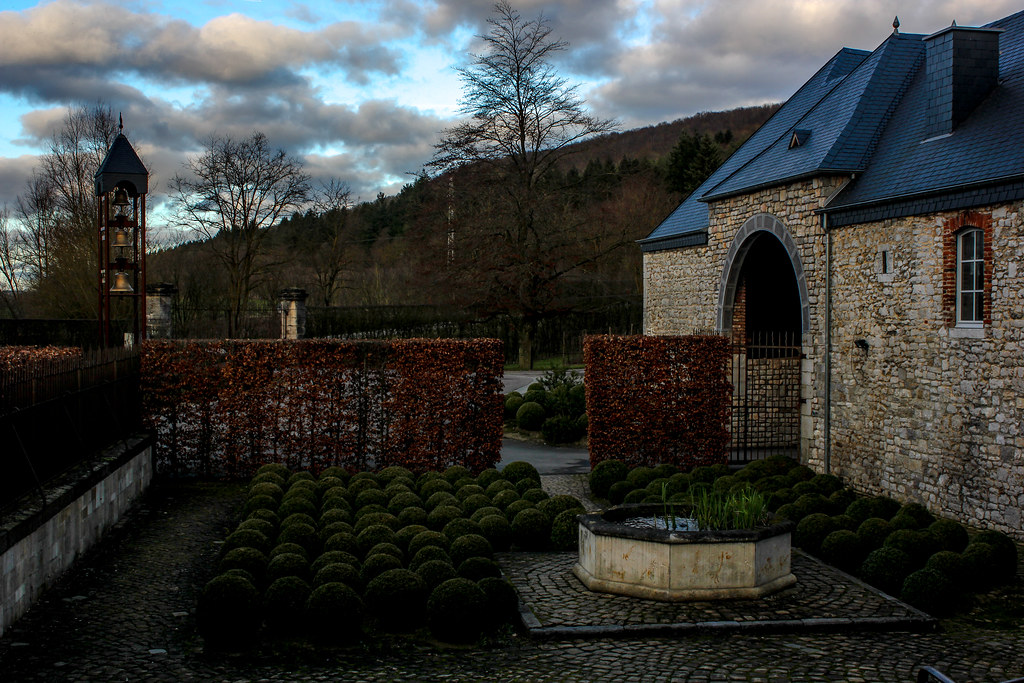 Vista del jardín de la Abadía de Rochefort con setos y fuente al atardecer.